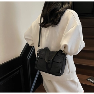 Rear view of a stylish black nylon crossbody bag worn by a model in a modern staircase