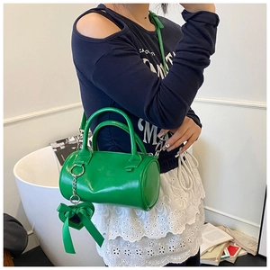 Detail of a bright green cylindrical Boston bag featuring a heart ribbon charm and shoulder strap