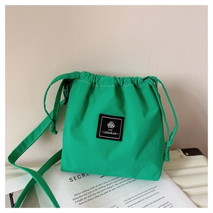 Detail of a bright green drawstring crossbody bag showing the square woven label and nylon fabric