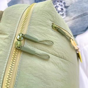Detail of light green nylon bag showing vibrant yellow zipper and precision stitching