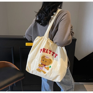 Detail of white canvas tote bag featuring plush bear embroidery and drawstring closure