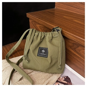 Detail of army green nylon drawstring crossbody bag with logo patch on wooden steps