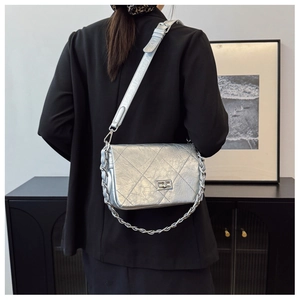 Silver quilted crossbody bag with metal chain strap worn on a black blazer jacket