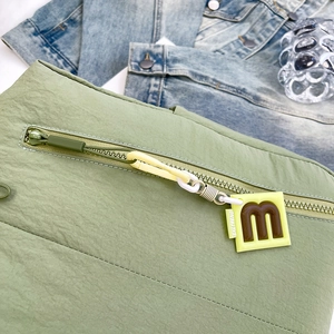Detail of light green textured nylon bag with letter m pendant and zipper closure