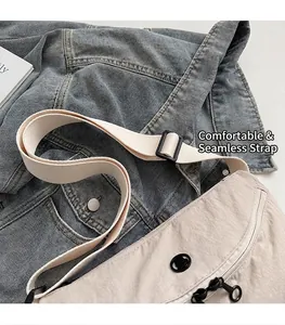 Detail of beige nylon crossbody bag with black zipper on blue denim background