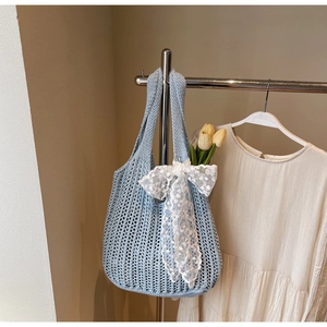 Detail of light blue crochet tote bag with a white lace bow and hollow knit texture