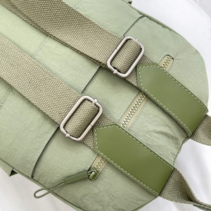 Detail of light green nylon backpack featuring widened fabric straps and silver metal buckles
