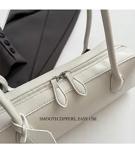Detailed close-up of smooth dual metal zippers on a cream leather underarm baguette bag
