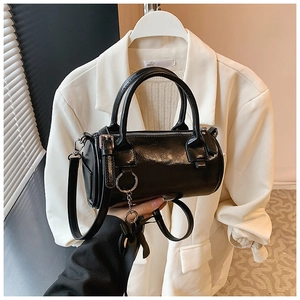 Detail of black cylindrical handbag with oil wax leather finish and ribbon charm