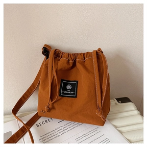 Detail of caramel canvas drawstring bucket bag with logo patch and contrast stitching