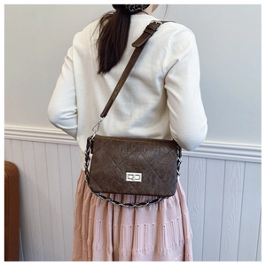 Detail of a dark brown quilted crossbody bag with silver twist lock and chain strap