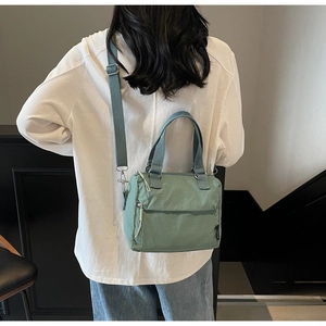Vue arrière du sac bandoulière en nylon vert haricot sur un modèle en intérieur moderne