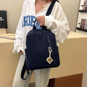 Detail showing deep blue nylon backpack texture with front zipper and decorative m-charm