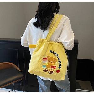 Detail view of a yellow drawstring tote bag featuring an embroidered cartoon bear and text