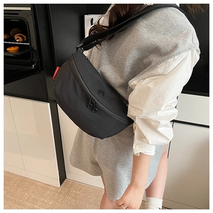 Close-up of black nylon half-moon crossbody bag with red label and dual ring zippers