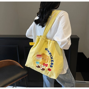 Detail of yellow canvas tote bag with embroidered cartoon bear and drawstring closure