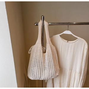 Detail of beige crochet tote bag with vertical woven hollow knit texture hanging on rack