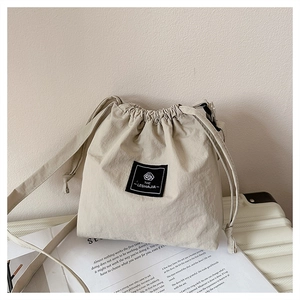 Close-up of beige nylon drawstring bucket bag with branded label on white suitcase