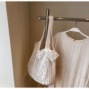 Close-up of beige crochet woven tote bag with a white lace bow on a metal hanger