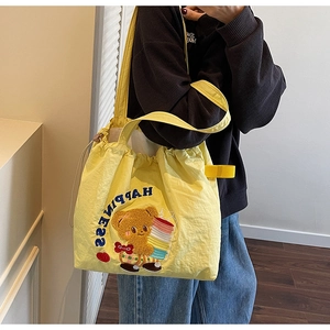 Detail of yellow tote bag featuring bear embroidery and blue Happiness text branding