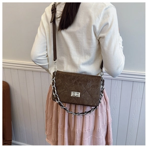 Detail of dark brown quilted crossbody bag with silver chain strap shown on a model