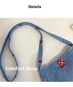 Détail du sac à bandoulière en denim bleu avec broderie cerise rouge et bandoulière