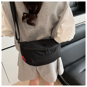 Back view of a model wearing a black nylon crescent crossbody bag with red label detail