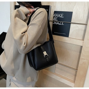 Détail d'un sac seau noir en cuir grainé avec boucle argentée sur un haut en maille douce