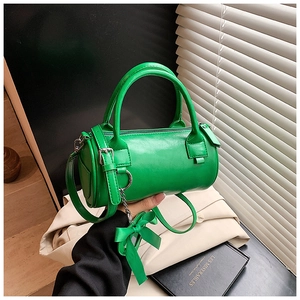 Dettaglio di una borsa a cilindro verde brillante con manico in pelle e ciondolo a fiocco
