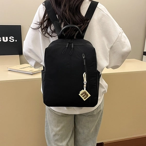 Close-up of black casual backpack featuring a stylish metal M charm and side pockets