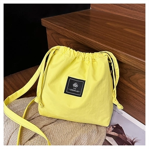 Detail of a bright yellow nylon drawstring crossbody bag with a black brand label