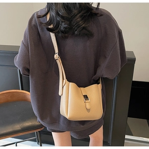 Détail d'un sac seau beige en cuir grainé avec bandoulière réglable sur le mannequin