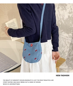 Détail du sac bandoulière en toile bleue avec broderie cerise rouge et fond incurvé