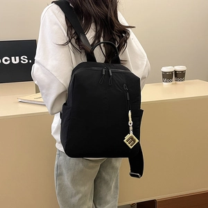 Detail of a minimalist black backpack featuring multiple pockets and a yellow charm accessory