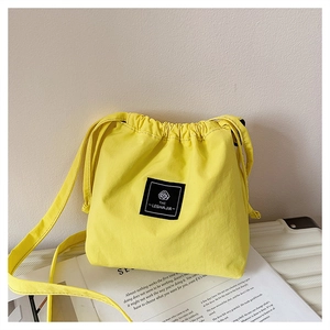 Close-up of bright yellow canvas drawstring bag with a black logo patch and shoulder strap