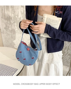 Détail du sac bandoulière en denim bleu avec broderie cerise et bouton à carreaux