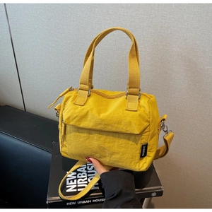 Détail d'un sac en toile jaune avec de larges poignées en tissu et un écusson logo