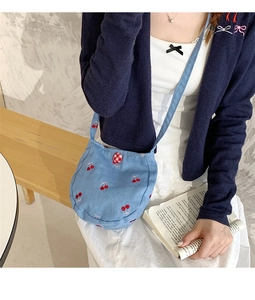 Détail du petit sac bandoulière en jean bleu clair avec broderies de cerises rouges