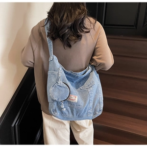 Détail du sac cabas en denim bleu avec porte-monnaie rond et étiquette sur un modèle