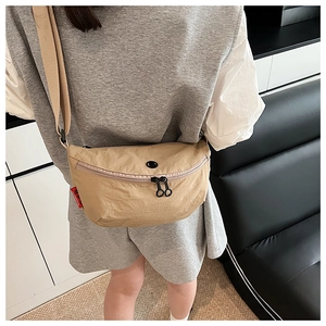 Detail view of khaki crescent crossbody bag with double zippers and red brand tag