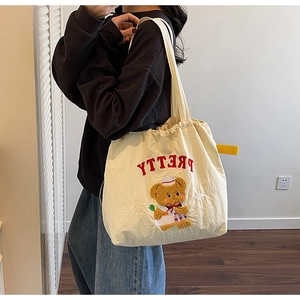 Detail of off-white tote bag featuring red PRETTY embroidery and a cute cartoon bear motif