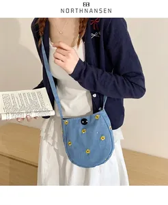 Détail d'un petit sac bandoulière bleu clair avec broderies fleurs jaunes et bouton noir