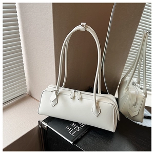 Detail of minimalist beige faux leather baguette bag with dual zippers on a book