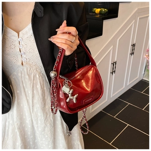Detail of red glossy patent leather bag with silver balloon dog charm and chain strap