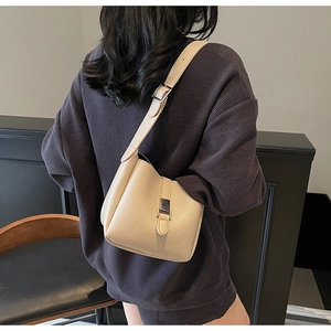 Détail du sac seau crème en cuir litchi porté sur un pull gris au style gaufre