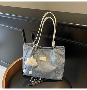 Détail du cabas en denim floral avec anses crème et accessoire de charme en nuage
