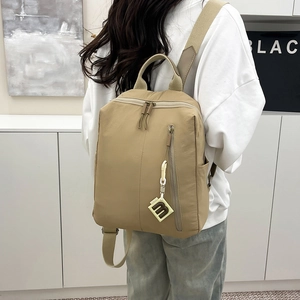 Khaki nylon backpack featuring top zipper and side pockets with decorative m-pendant