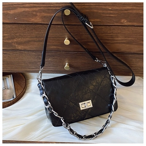 Detailed close-up of a quilted black leather handbag with silver turn-lock and chain strap