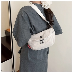 Detail view of cream white nylon crossbody bag with dual black zippers and red side tag