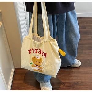 Detail of cream yellow canvas tote bag featuring 3D plush bear embroidery and Pretty text